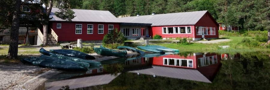 Nesholmen Leirstad ved Eimhjellvatnet — raud trebygning med kanoar ved vatnet